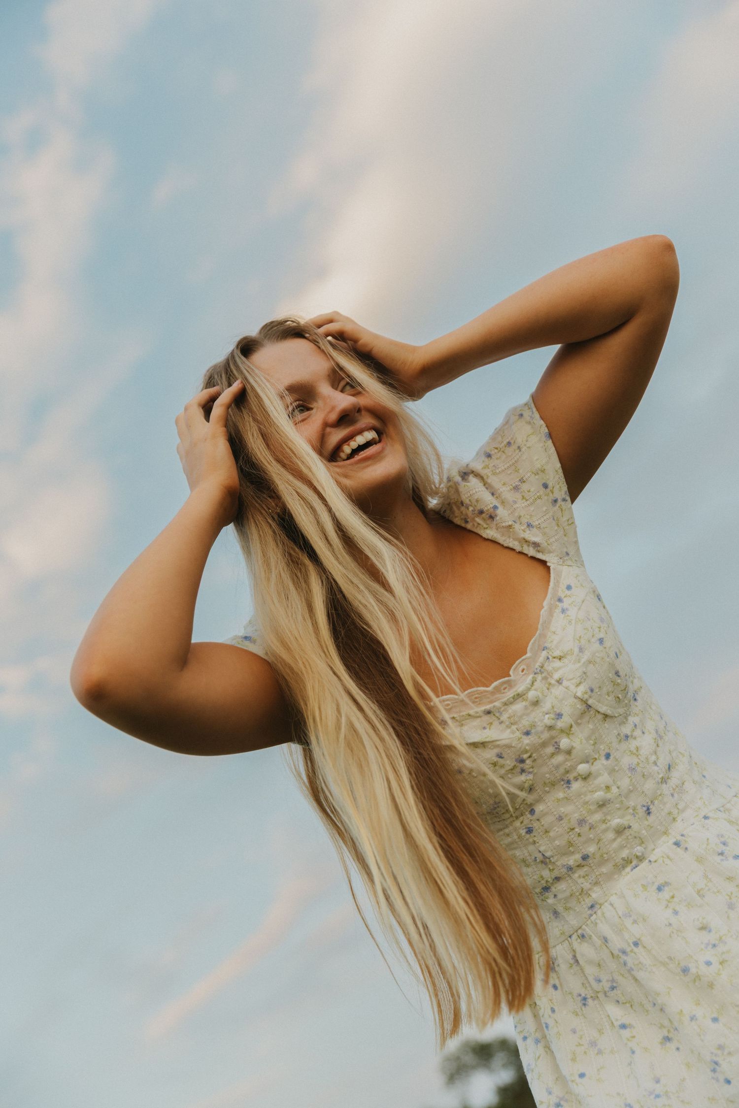 Woman in white dress with flowing blonde hair against blue sky.