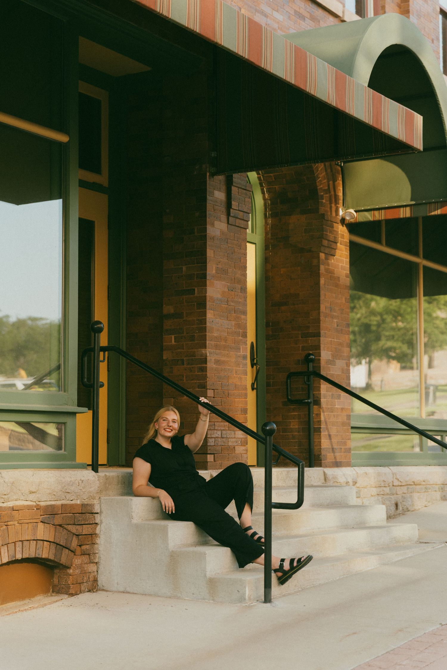 Person in black outfit sitting on concrete steps outside brick building.