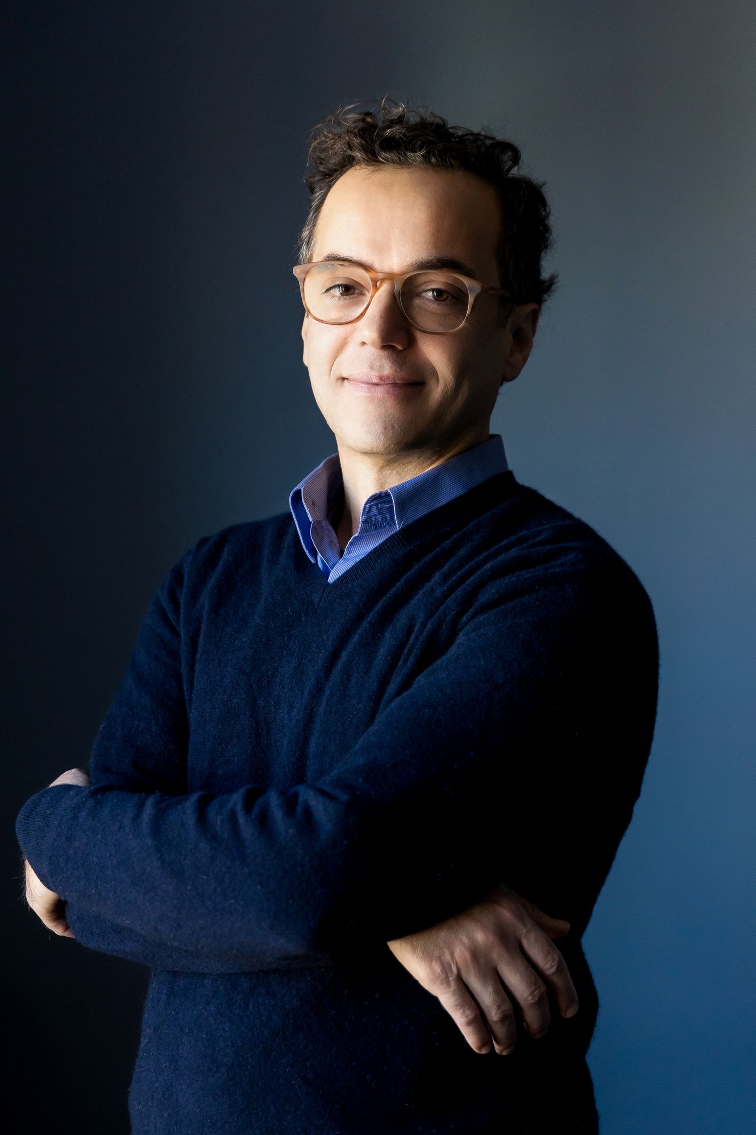 Professional portraits of a person in a navy sweater against a dark blue backdrop.