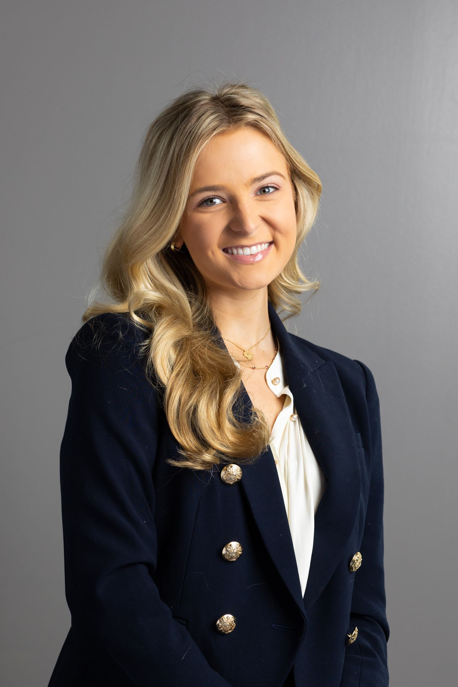 Corporate headshots of a person in a navy blazer with gold buttons against a grey background.