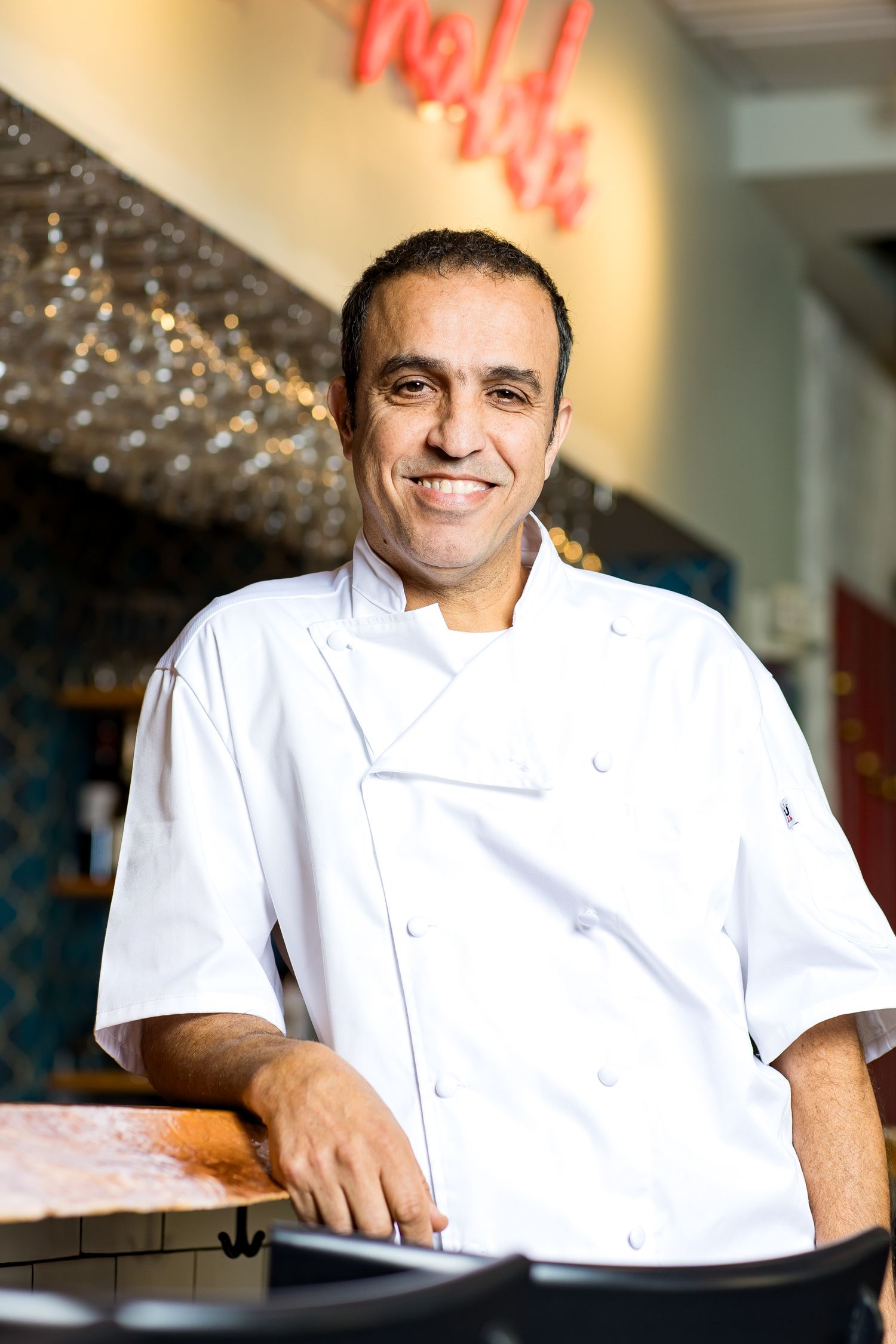 Chef in white uniform smiling while sitting in a restaurant kitchen.