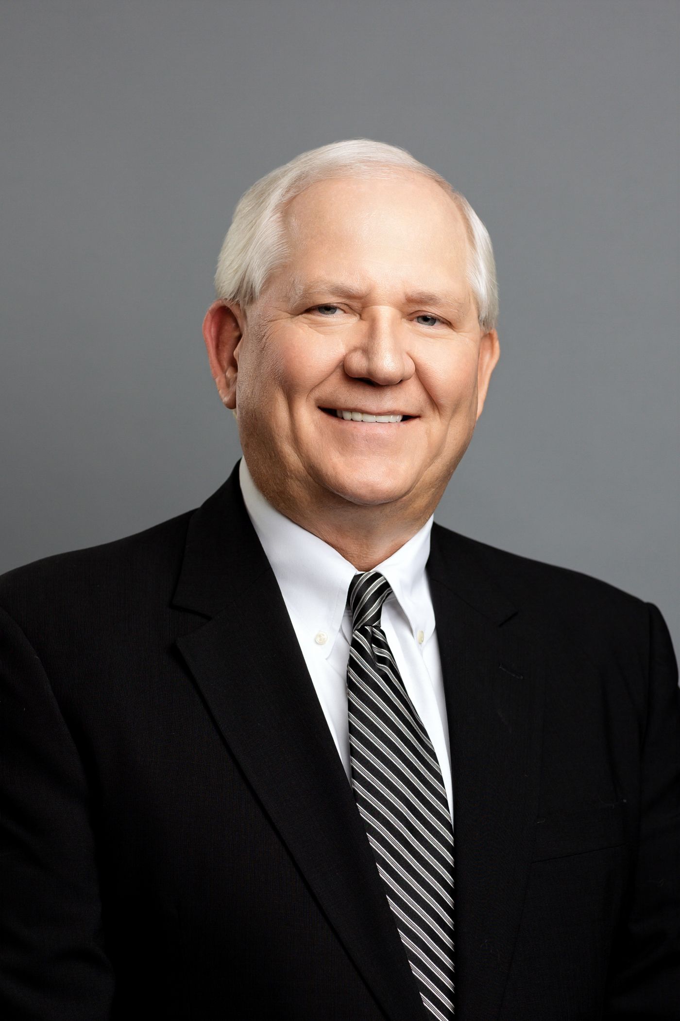 Professional headshot series of person in dark suit and striped tie against gray backdrop.