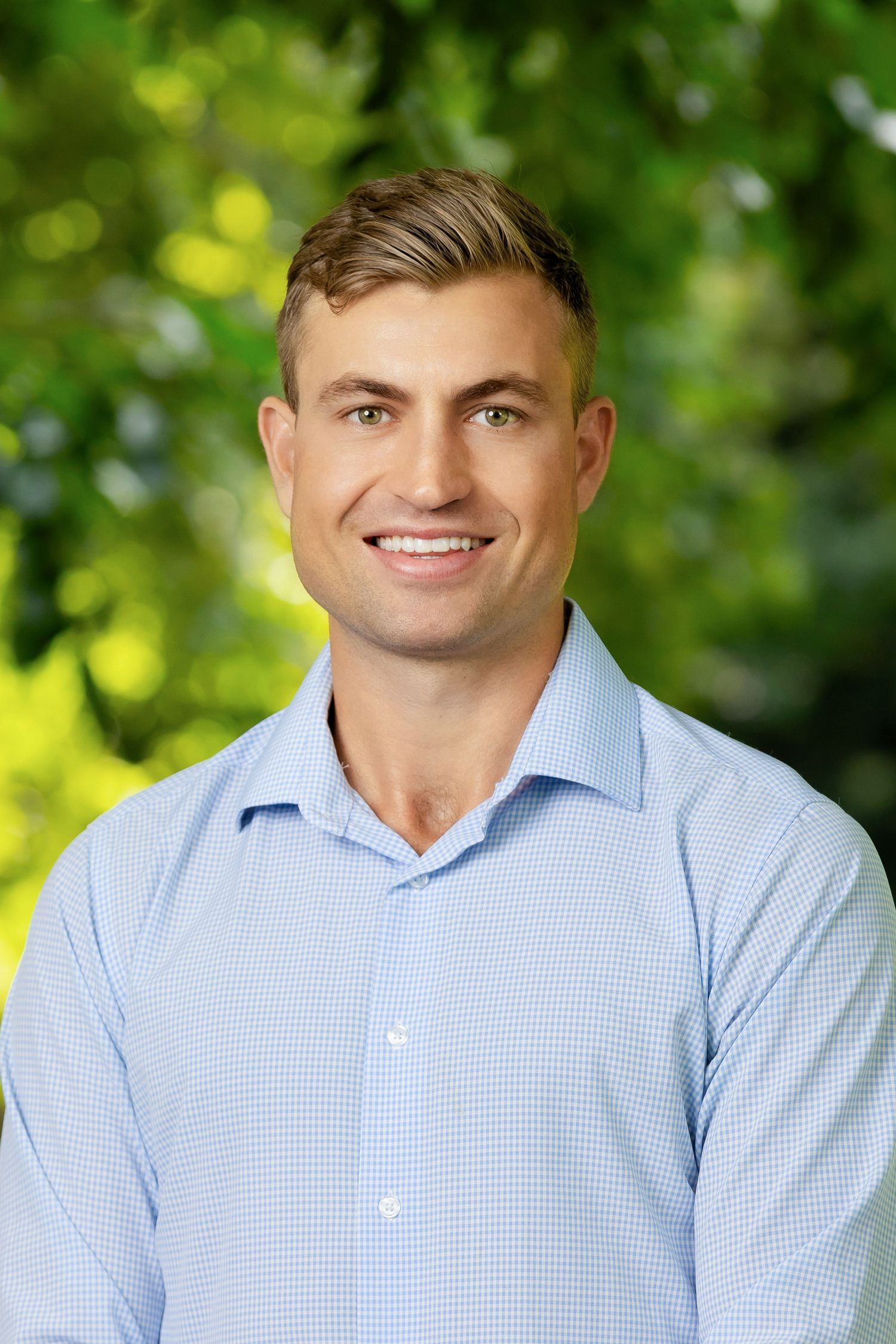 Professional headshot series in light blue checkered shirt against natural outdoor setting.