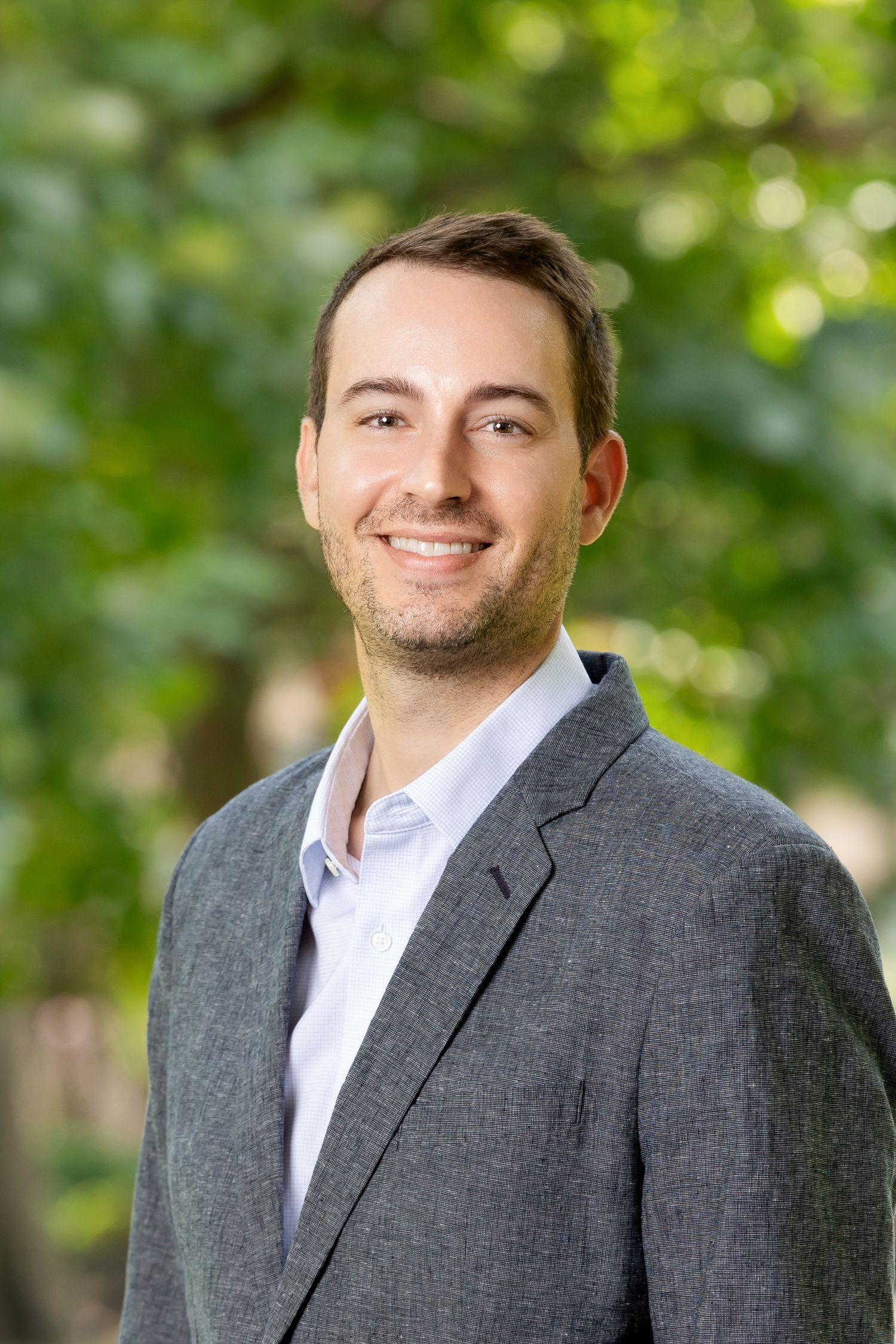 Professional headshot series in gray suit jacket and white shirt against blurred green background.