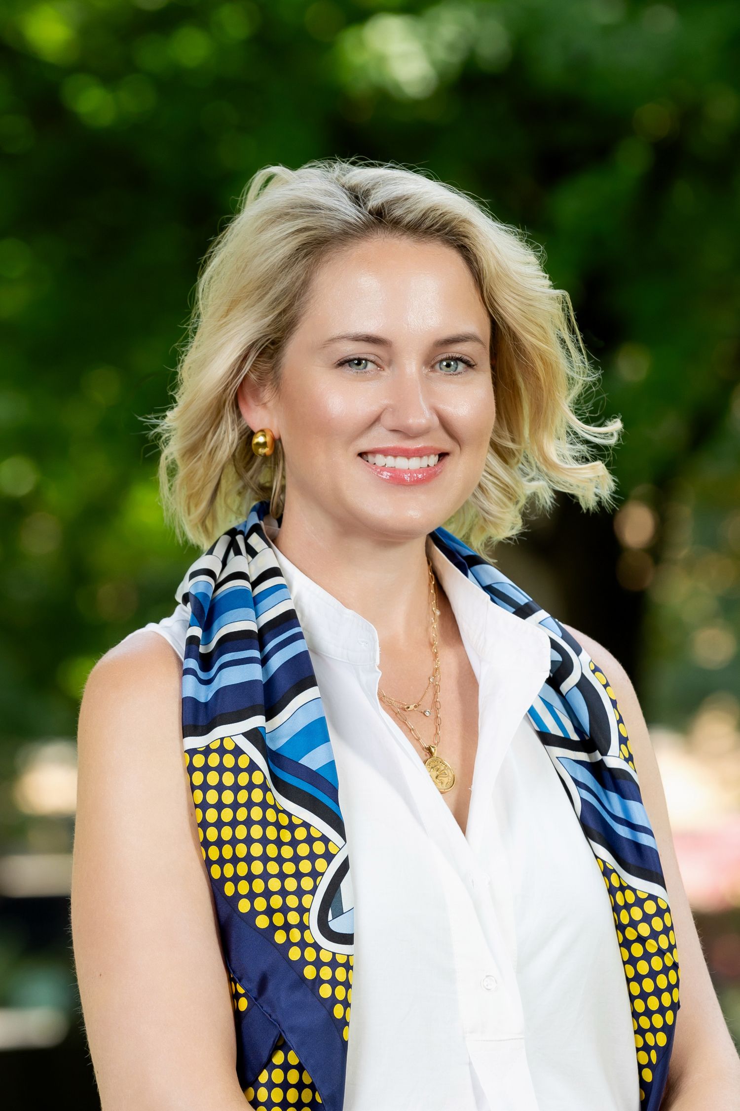 Professional headshot of a person wearing a navy and yellow patterned top with a white collar against a green background.