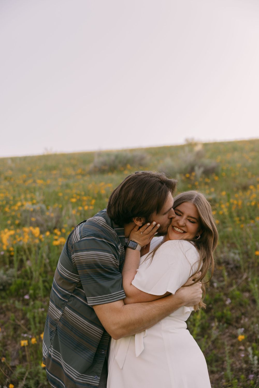 Couple sharing an intimate moment in a field of yellow wildflowers at sunset.