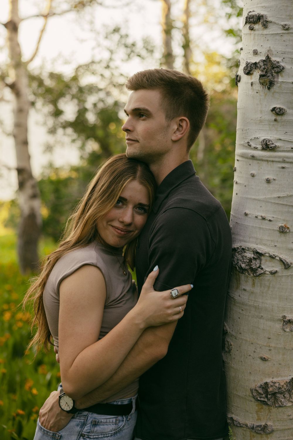 A couple embraces beside a white birch tree in golden evening light.