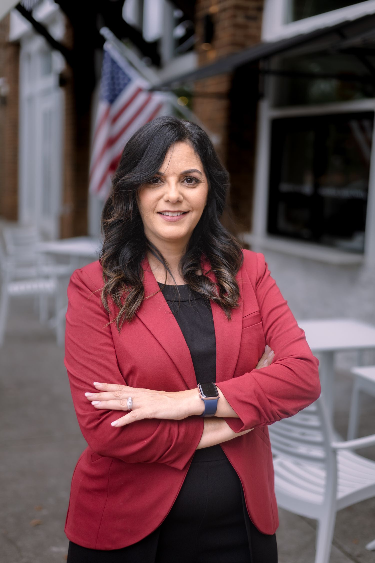 Professional headshots in red blazer against brick building with American flags.
