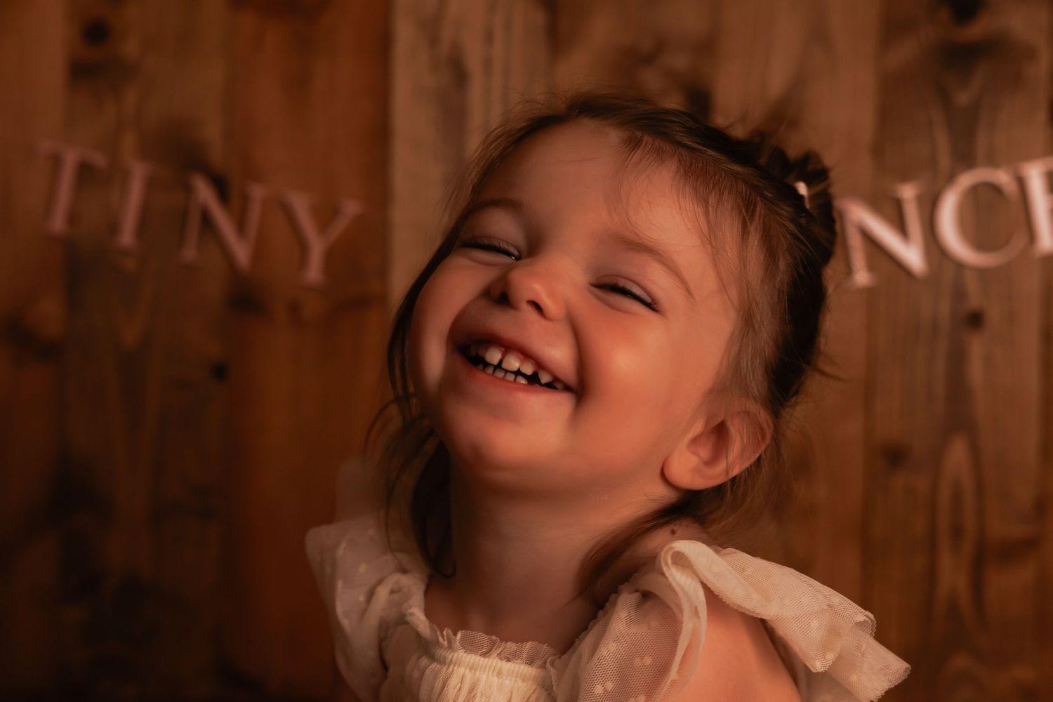 Baby lying on soft white fur against wooden backdrop in cozy indoor setting.
