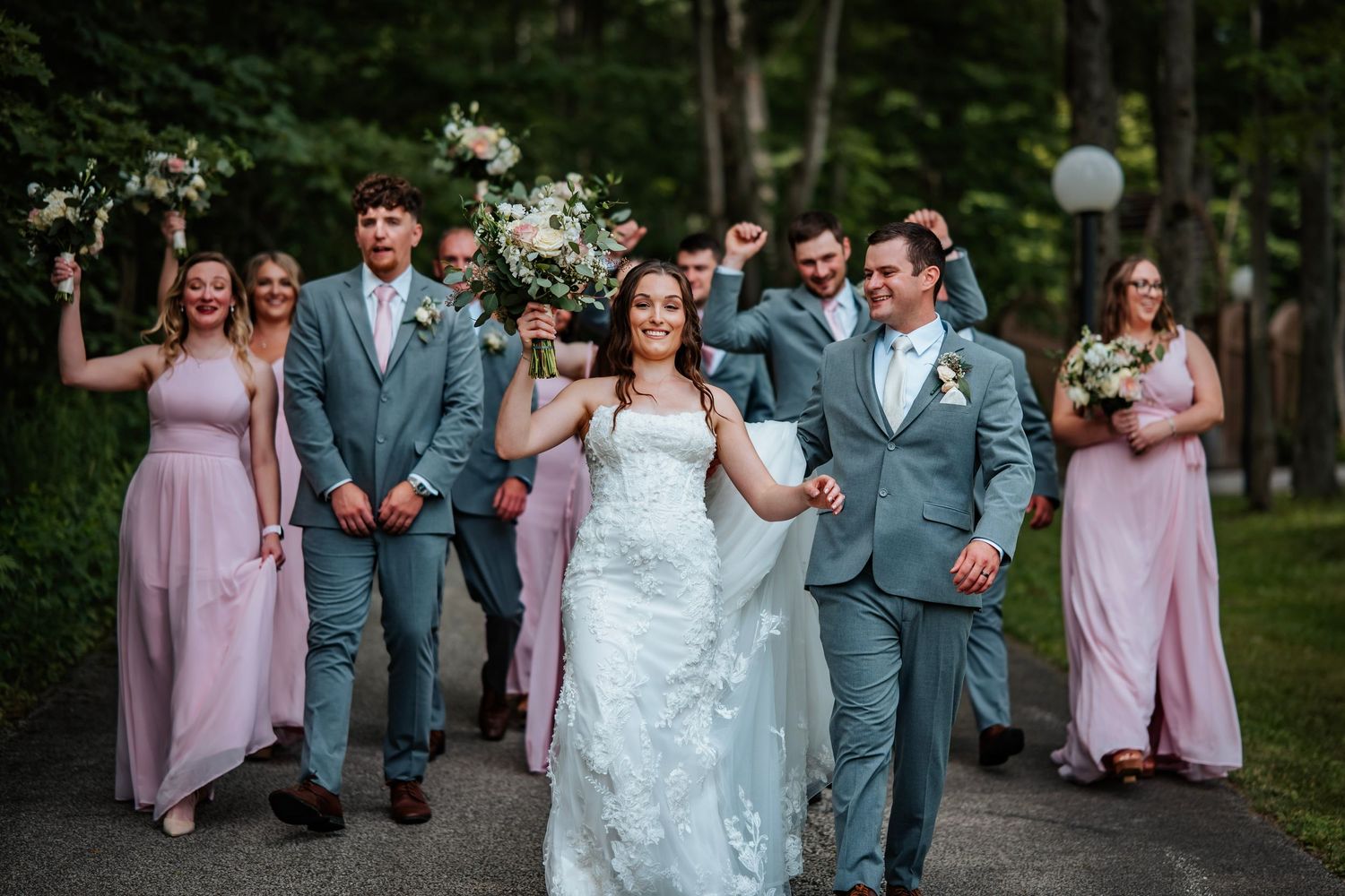 Newlyweds pose dramatically in tall grass during sunset with bride's dress flowing.