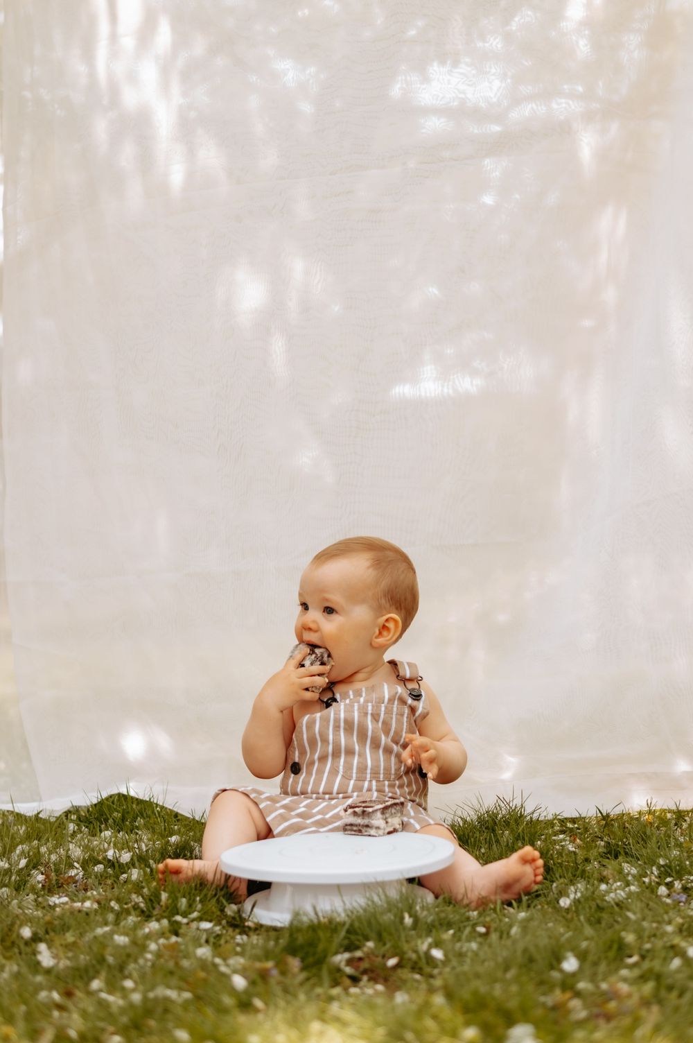 Baby in brown striped outfit having cake smash photo session outdoors.