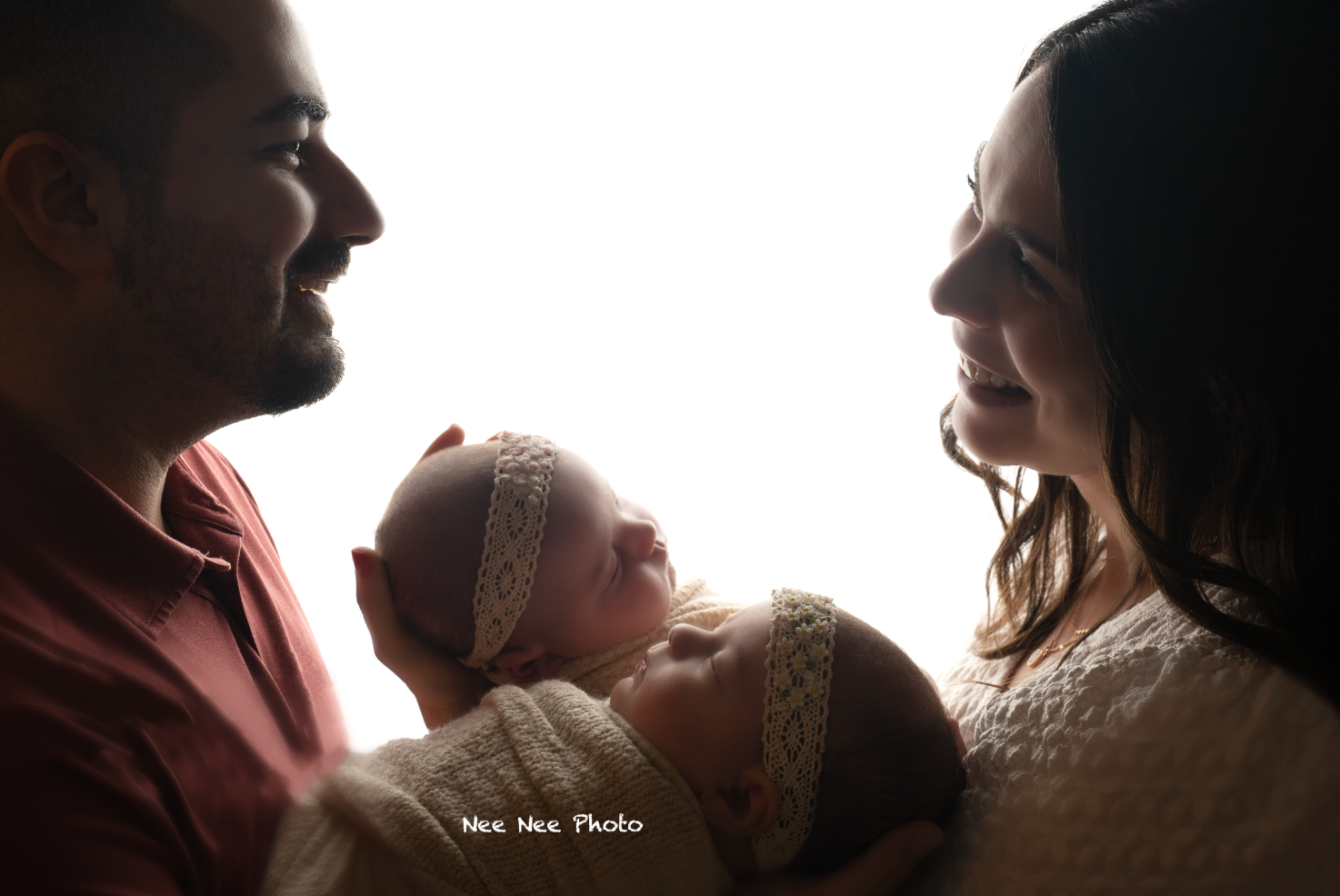New parents lovingly gaze at their swaddled newborn baby in a beautiful backlit portrait photo. Embracing Life’s Beauty