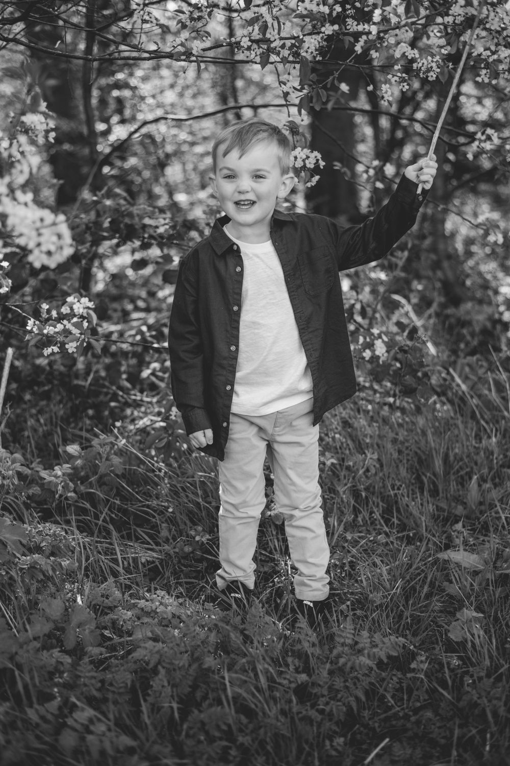 Black and white photo of child laughing while standing under flowering trees.