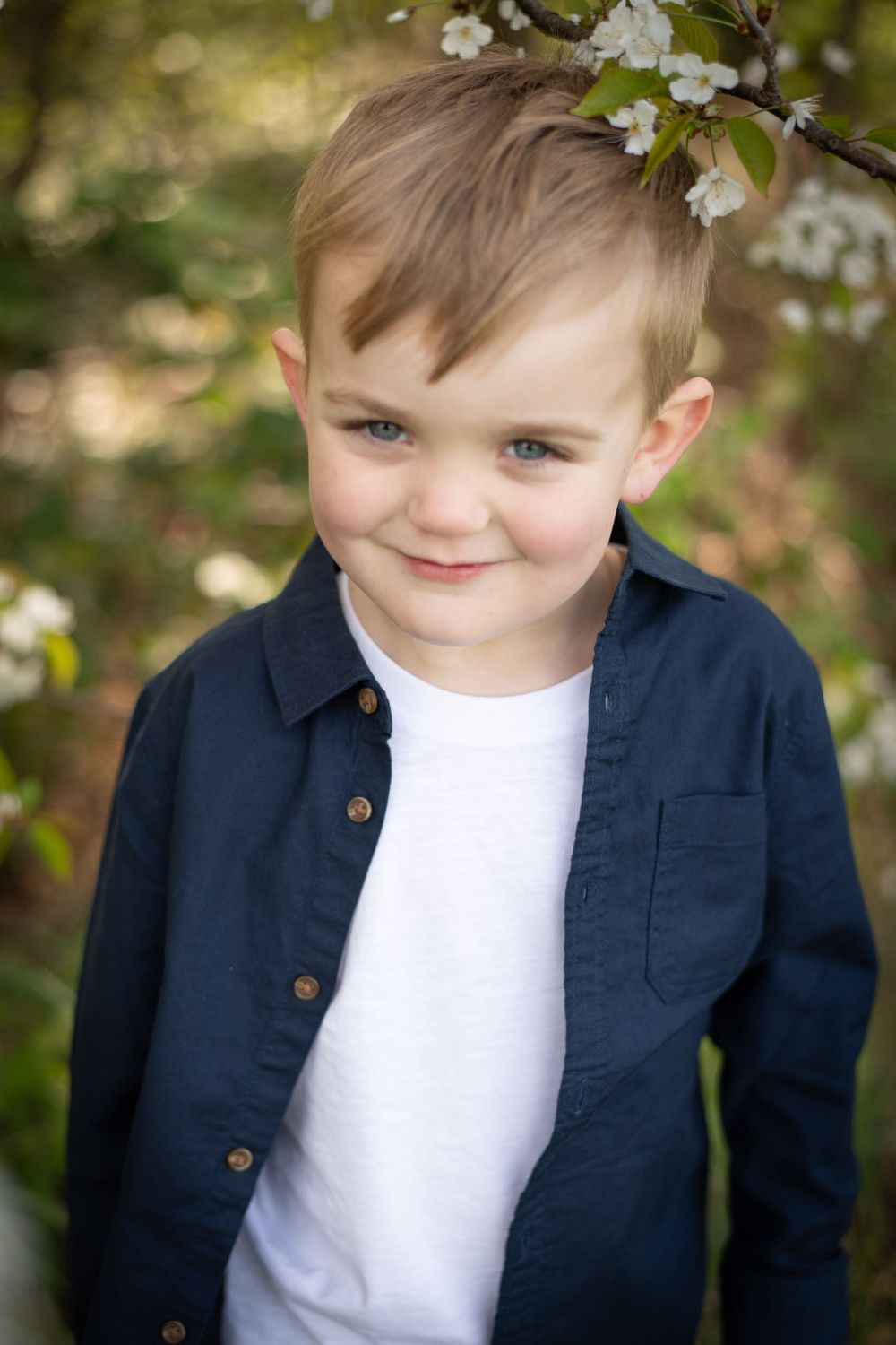 Portrait of child wearing navy button-up shirt and white t-shirt under flowering spring tree.