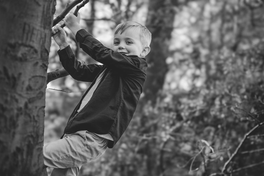 Black and white action shot of child climbing tree in natural setting.