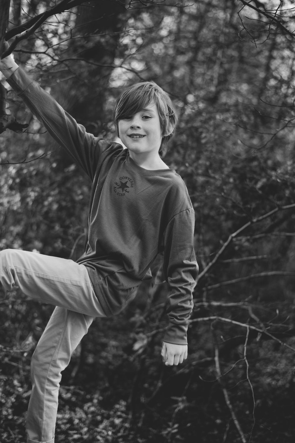 Child in casual wear striking playful pose while balancing on one leg outdoors.