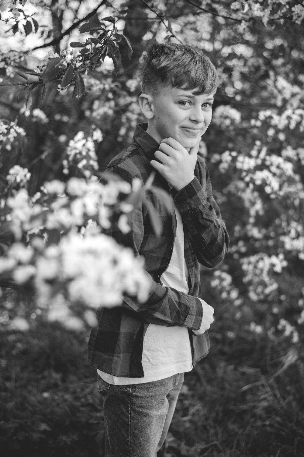 Black and white lifestyle portrait of youth posing thoughtfully among blooming branches.