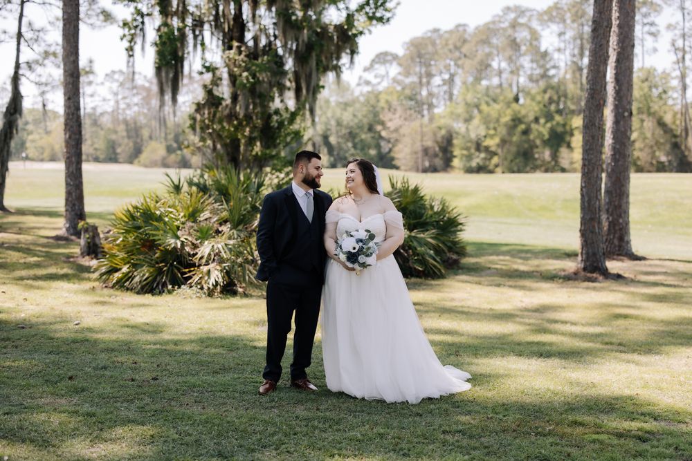 Bride and groom share a romantic moment on lush green lawn surrounded by Spanish moss-draped trees.