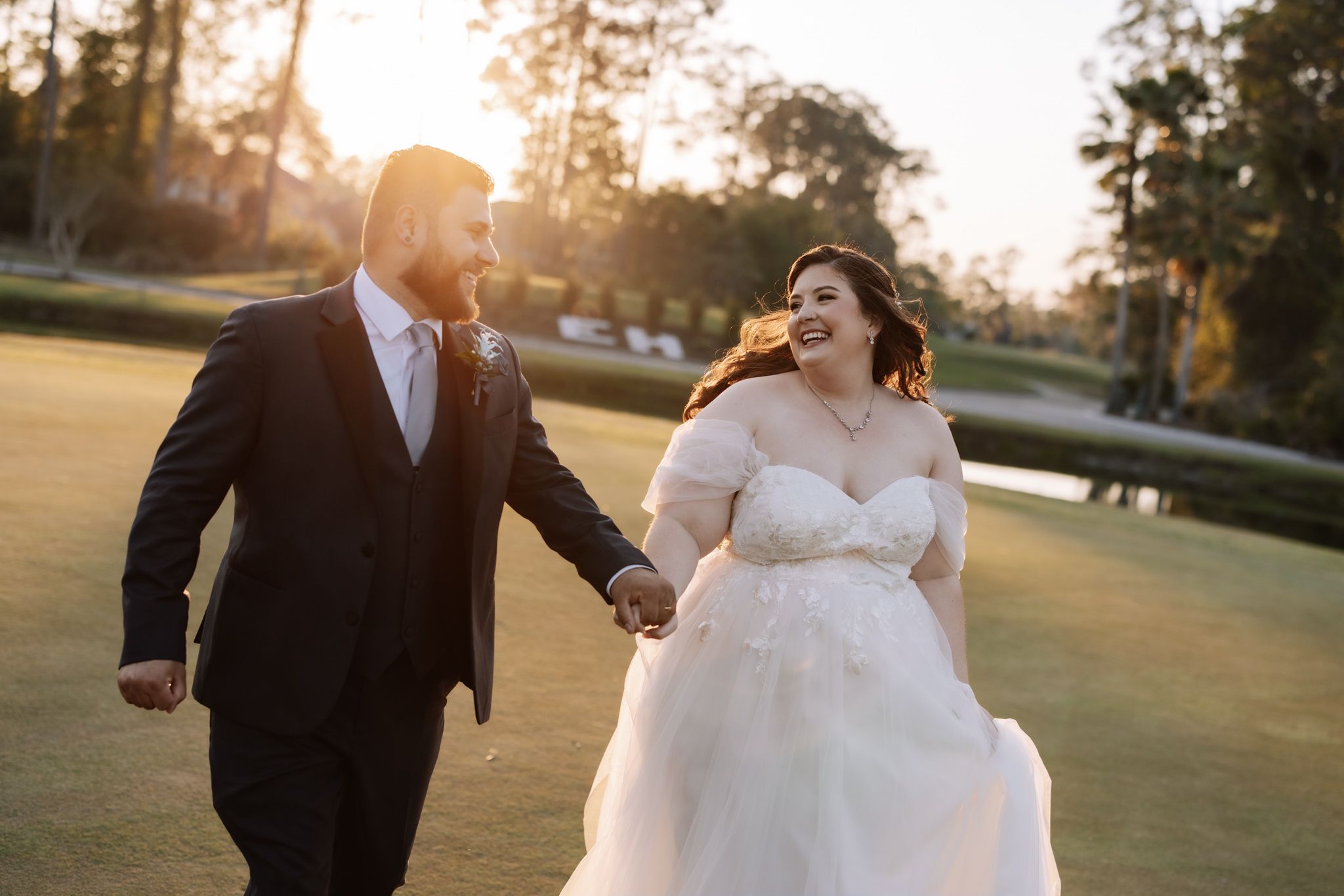 Bride and groom holding hands running through golf course at golden hour sunset in elegant wedding attire.