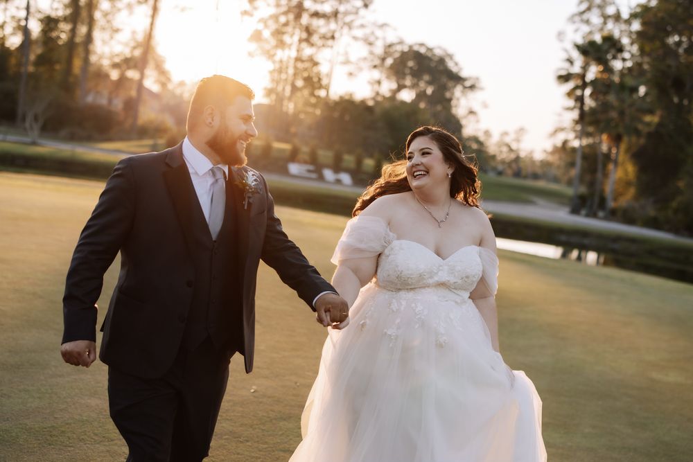 Bride and groom holding hands running through golf course at golden hour sunset in elegant wedding attire.