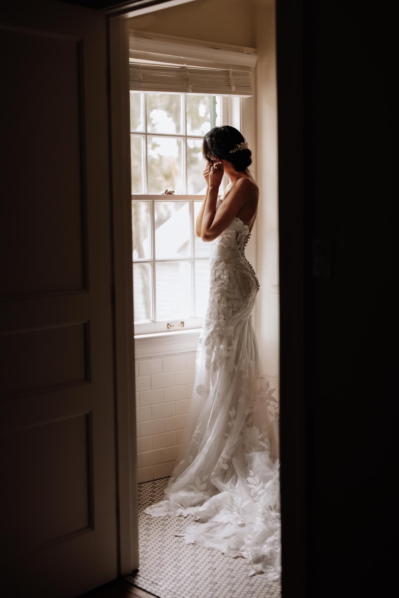 A sequence of moody silhouette photos showing a bride in a lace wedding gown looking out a bright window.