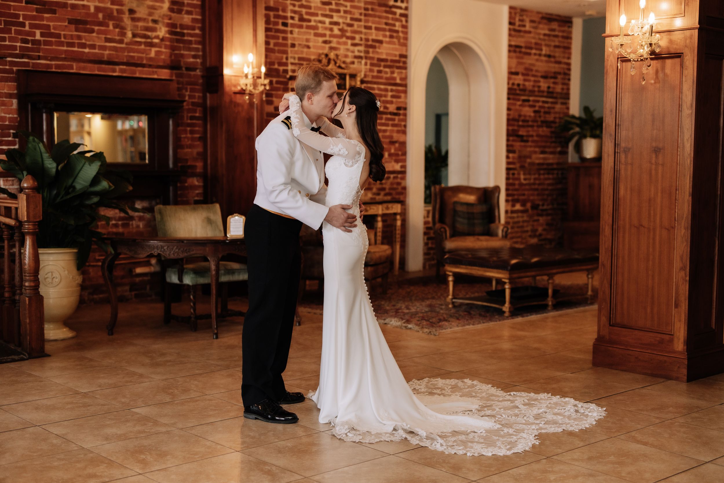 Bride and groom share romantic embrace in elegant venue with exposed brick walls and warm lighting.