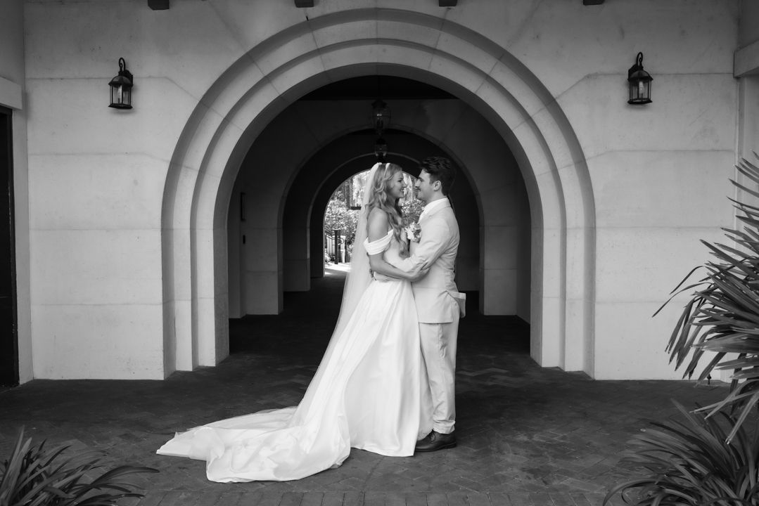 A romantic black and white wedding moment captured under an elegant arched doorway.
