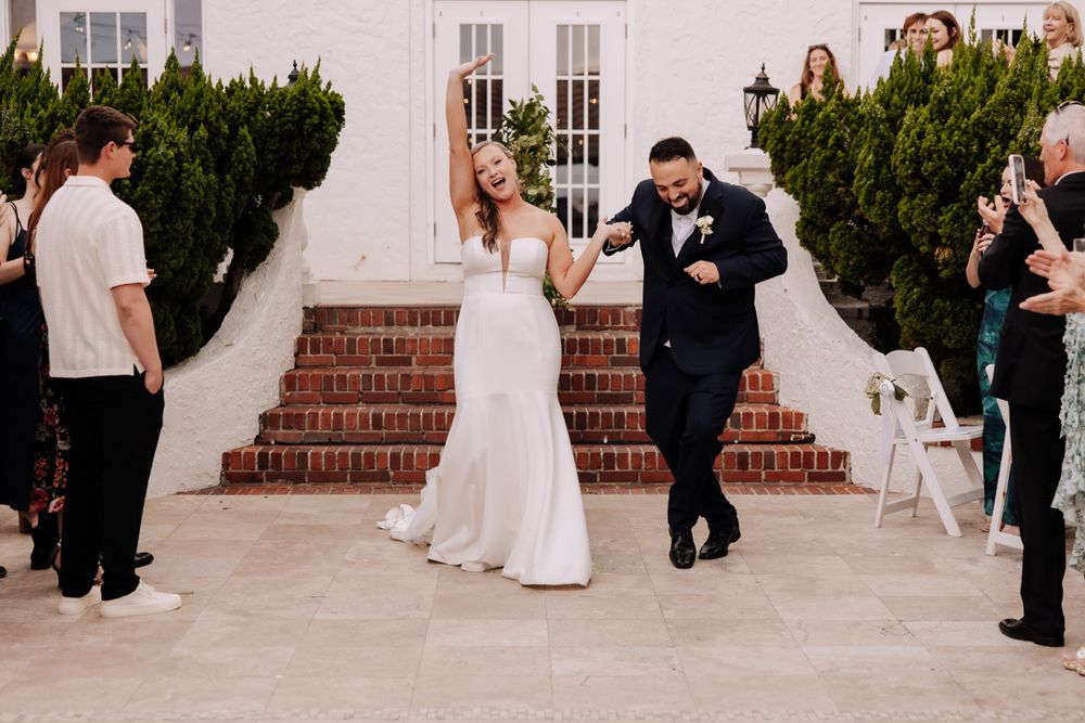 Joyful newlyweds celebrate as they descend white brick steps together at an elegant venue entrance at casa marina jax beach