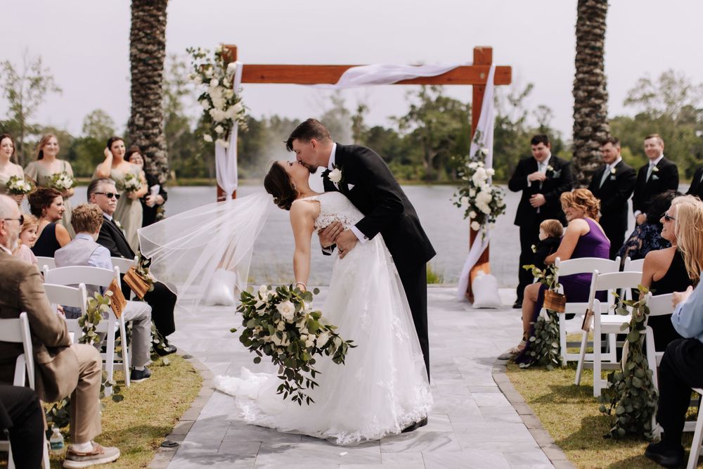 Wedding ceremony with guests watching couple share their first kiss under an outdoor arch.