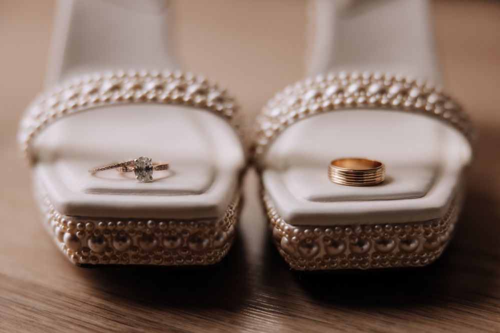 Wedding rings displayed elegantly on white bridal shoes with pearled embellishments and ornate detailing.
