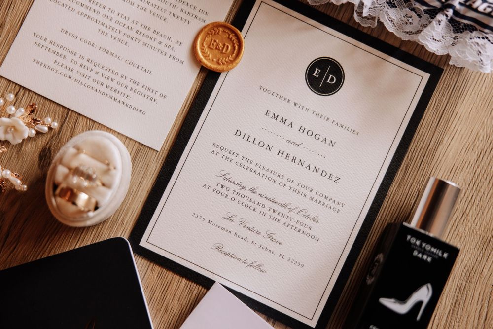 Wedding stationery flatlay featuring black and white invitation with wax seal and perfume bottle.
