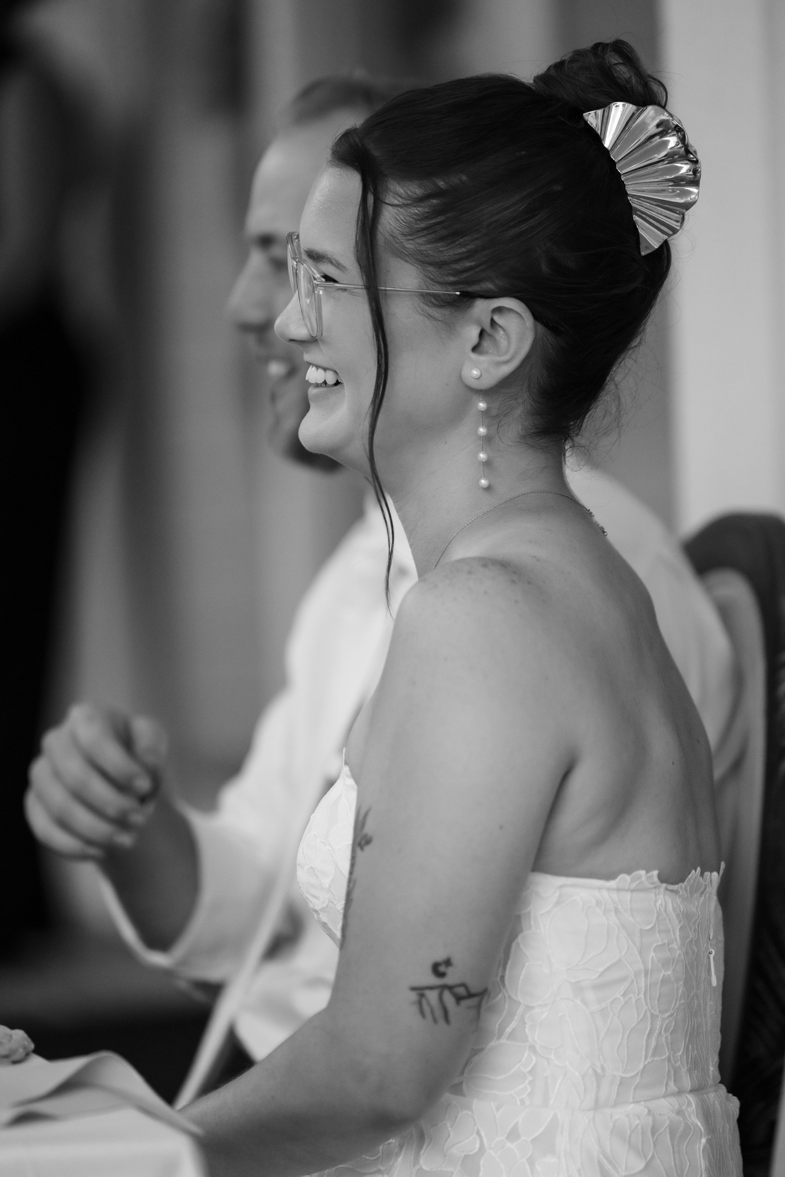 Black and white photo of a smiling bride in a strapless dress with pearl earrings and hair accessory at her wedding.