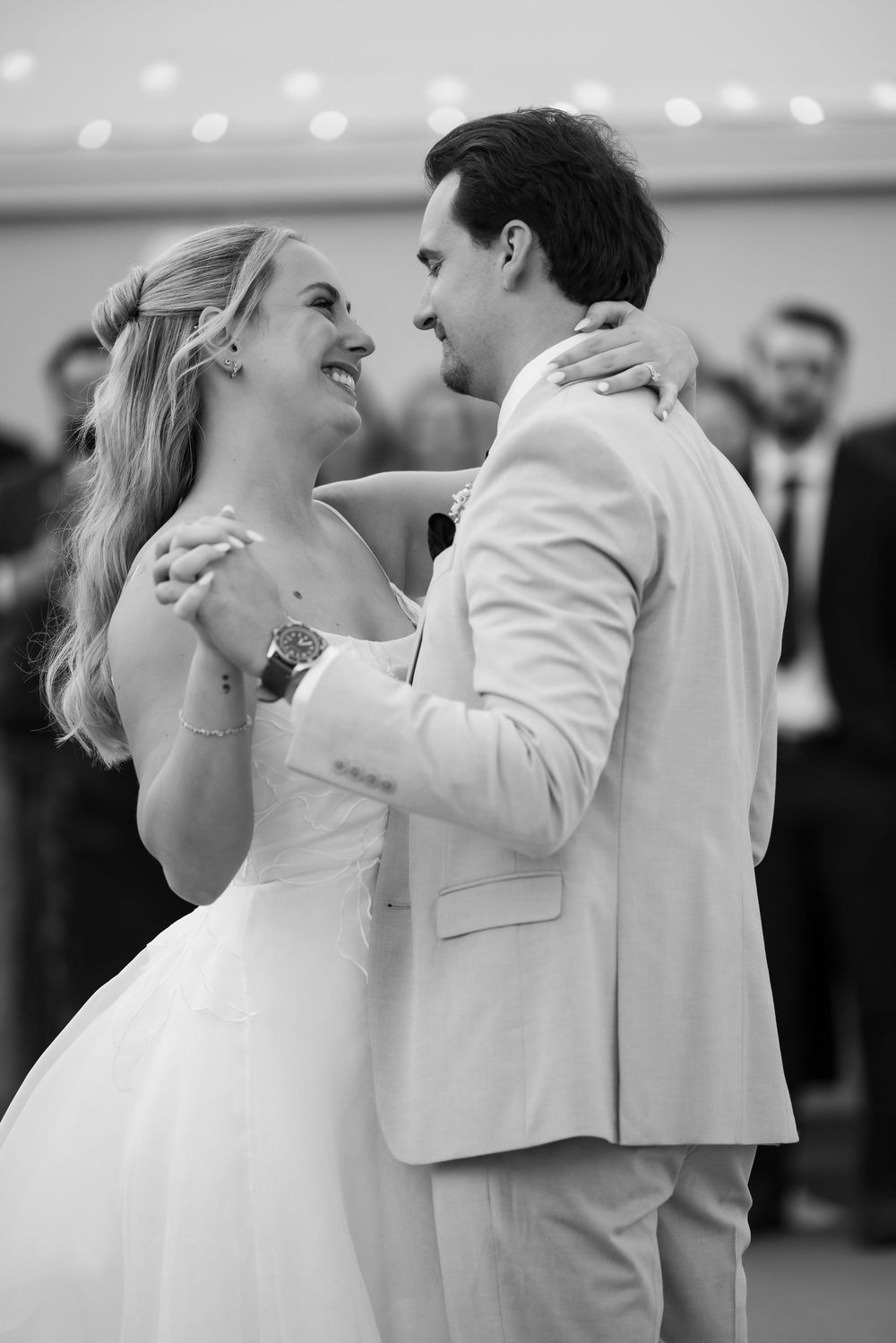 Black and white photo of bride and groom sharing their first dance, smiling at each other at wedding reception.