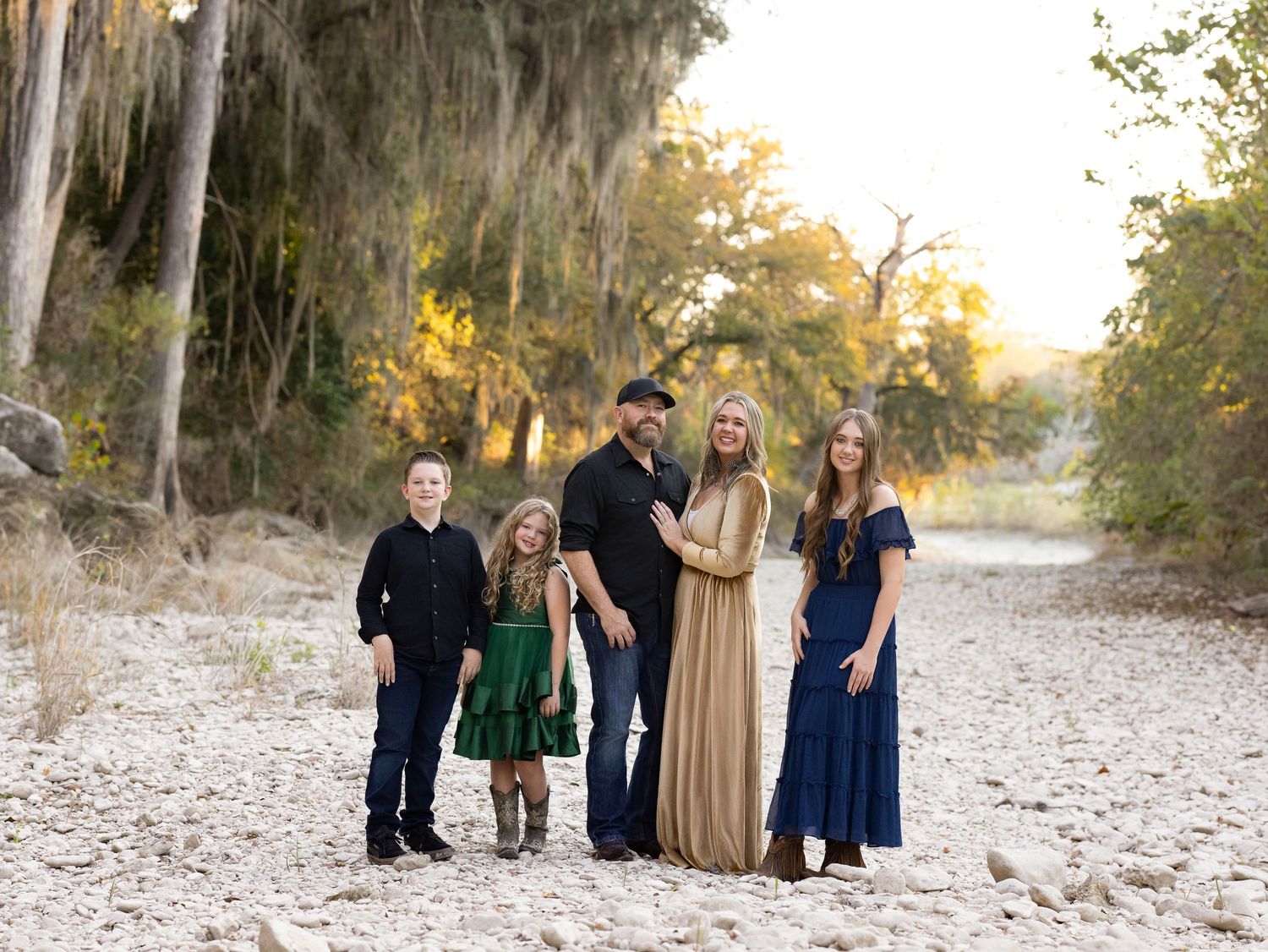 A young family in coordinated formal attire poses together on a rock bar during golden hour sunset.