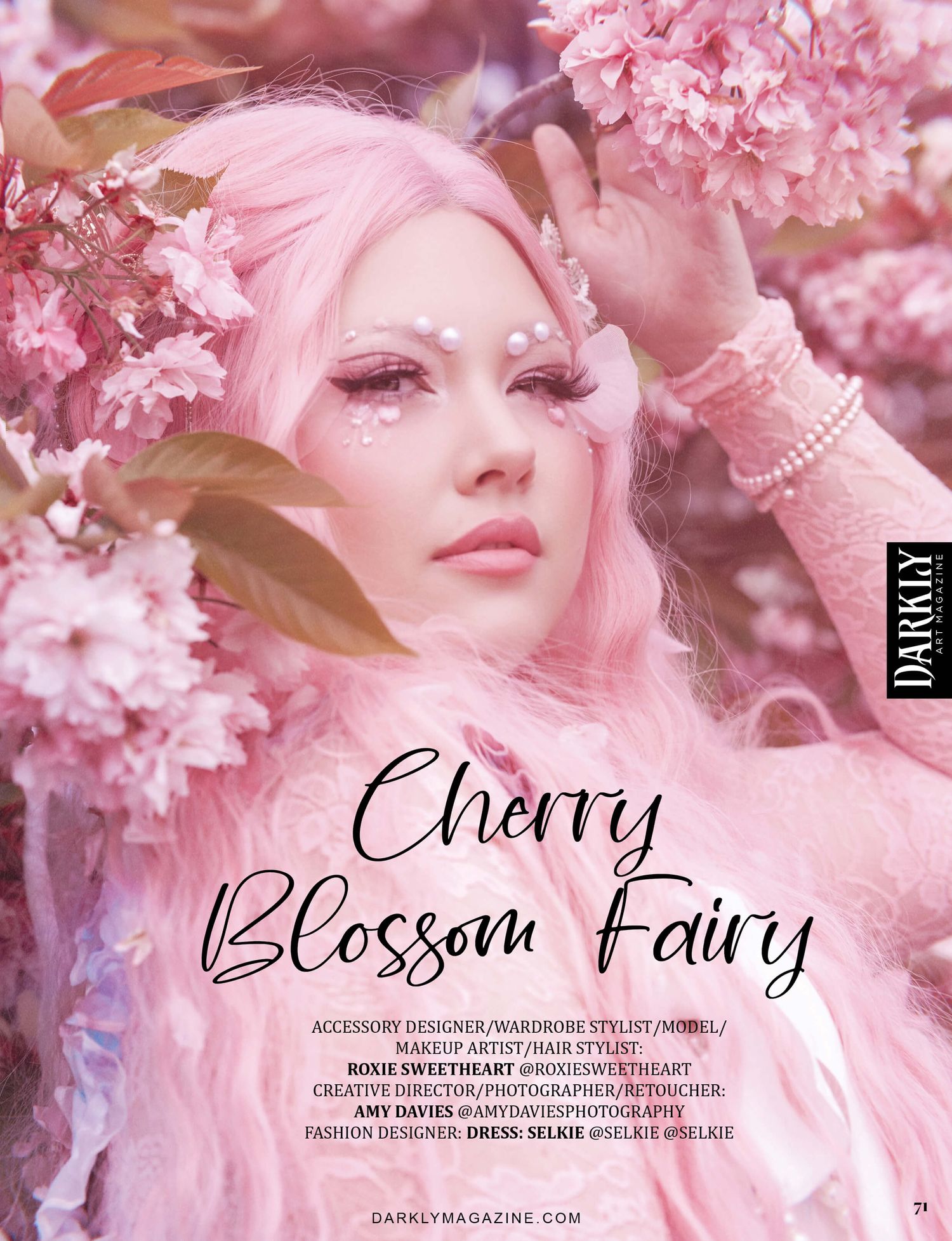 woman dressed as a “Cherry Blossom Fairy” with pink hair and floral accessories, surrounded by cherry blossoms.
