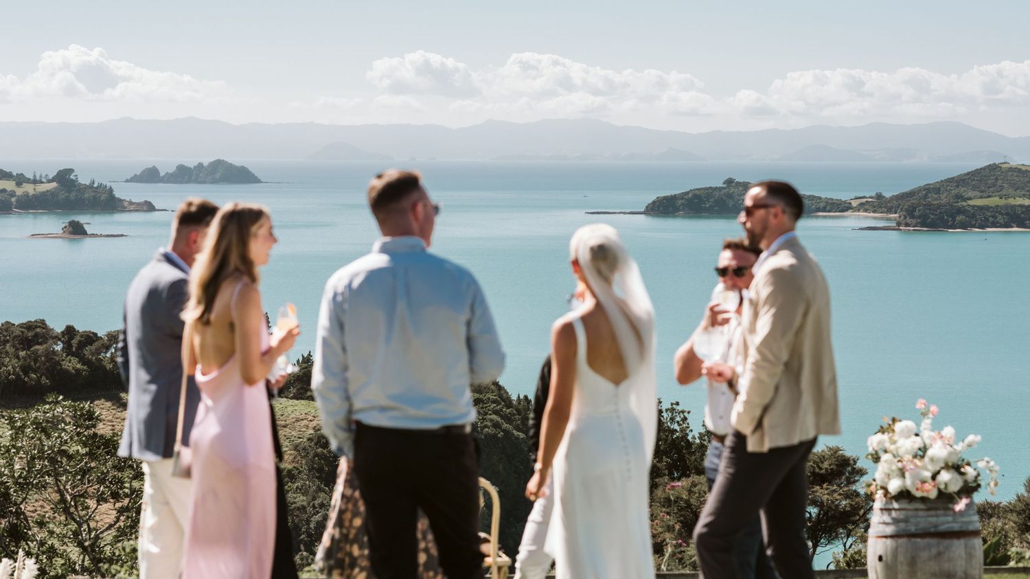 A scenic wedding gathering overlooking a tropical bay with islands and blue waters under cloudy skies.