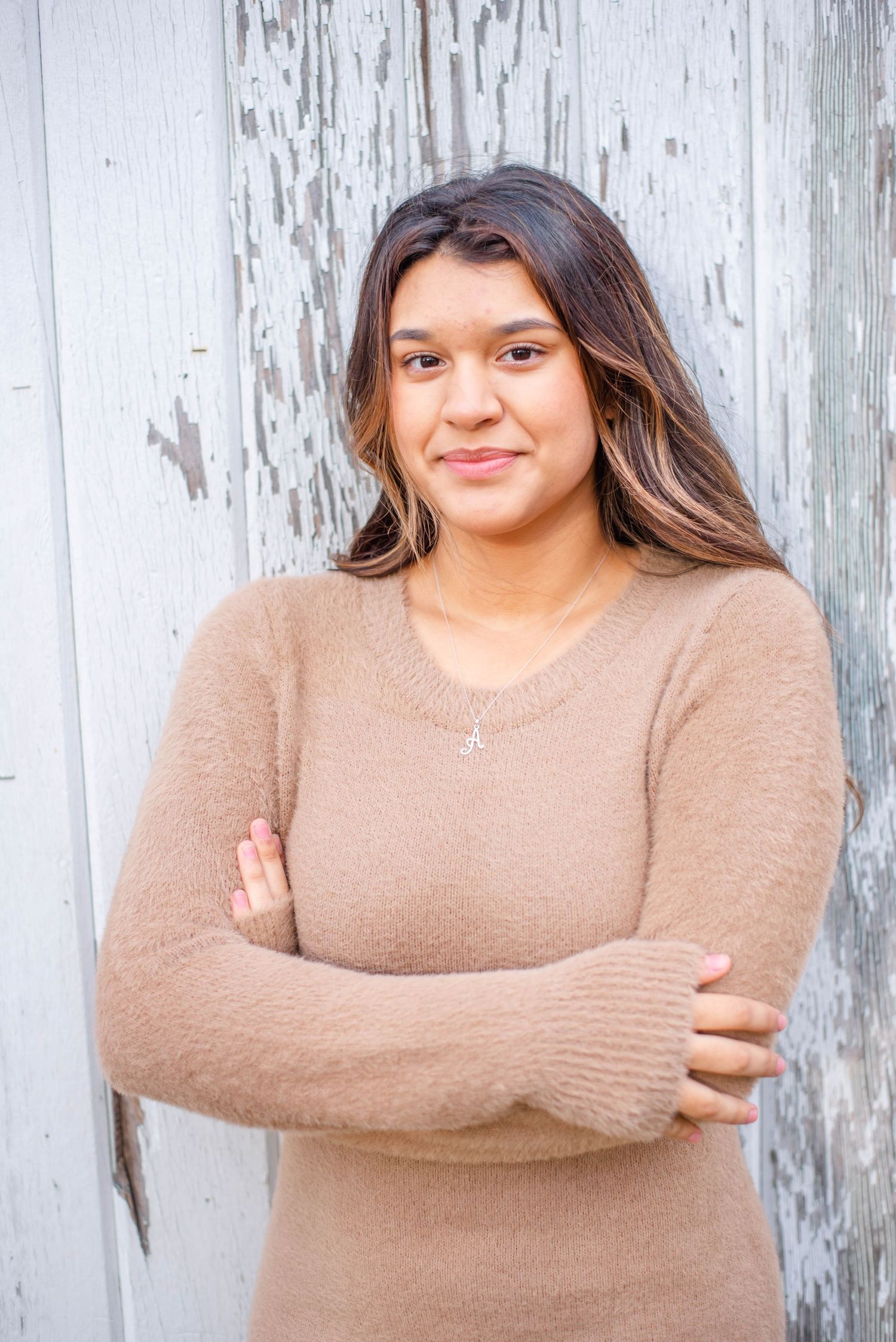 Portrait against weathered white wall showing woman in beige sweater dress with arms crossed.