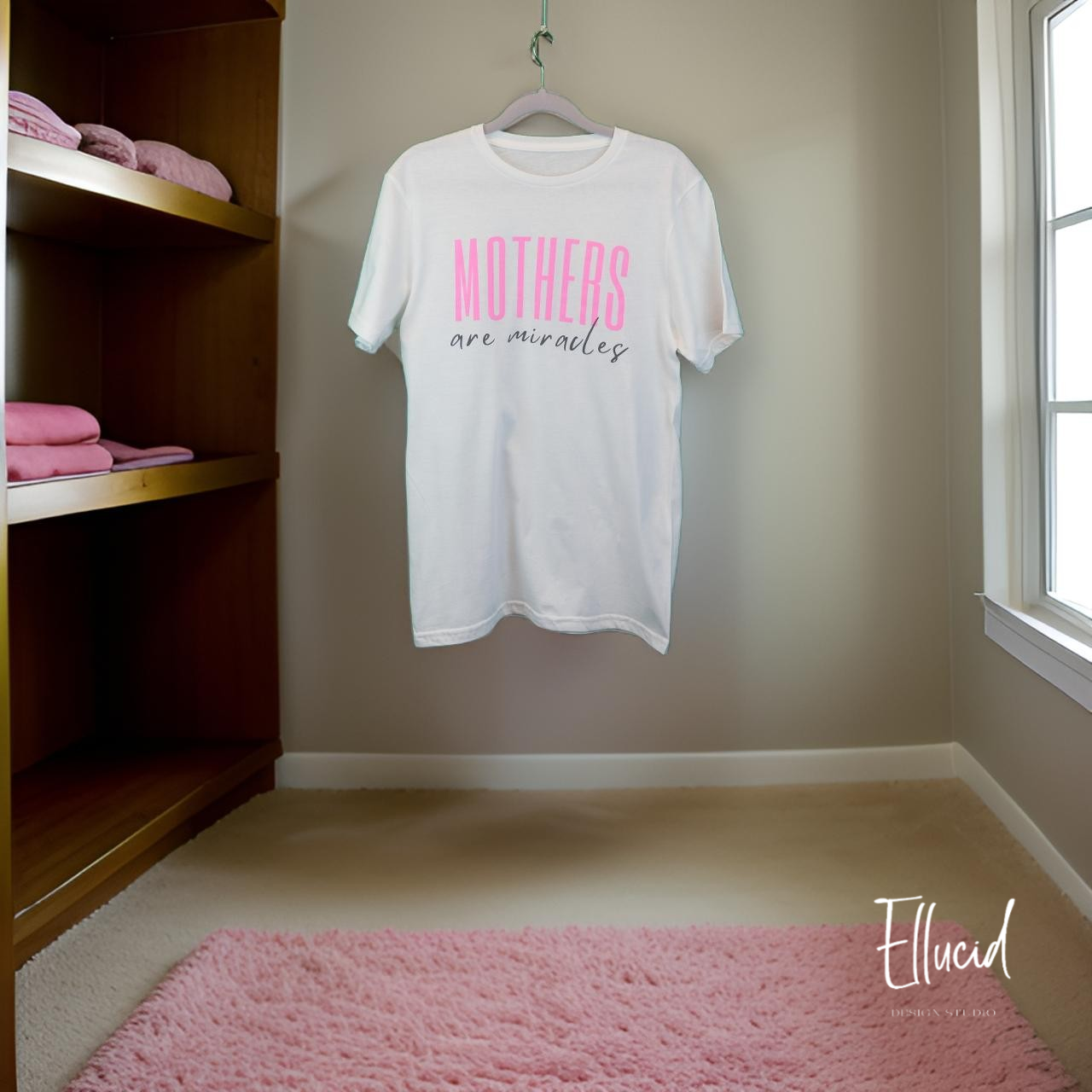 White t-shirt with pink text hanging on wall above pink rug in minimal room setting.