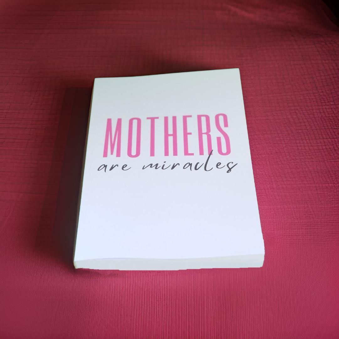 White notecard with pink text reading 'Mothers are miracles' on burgundy background.