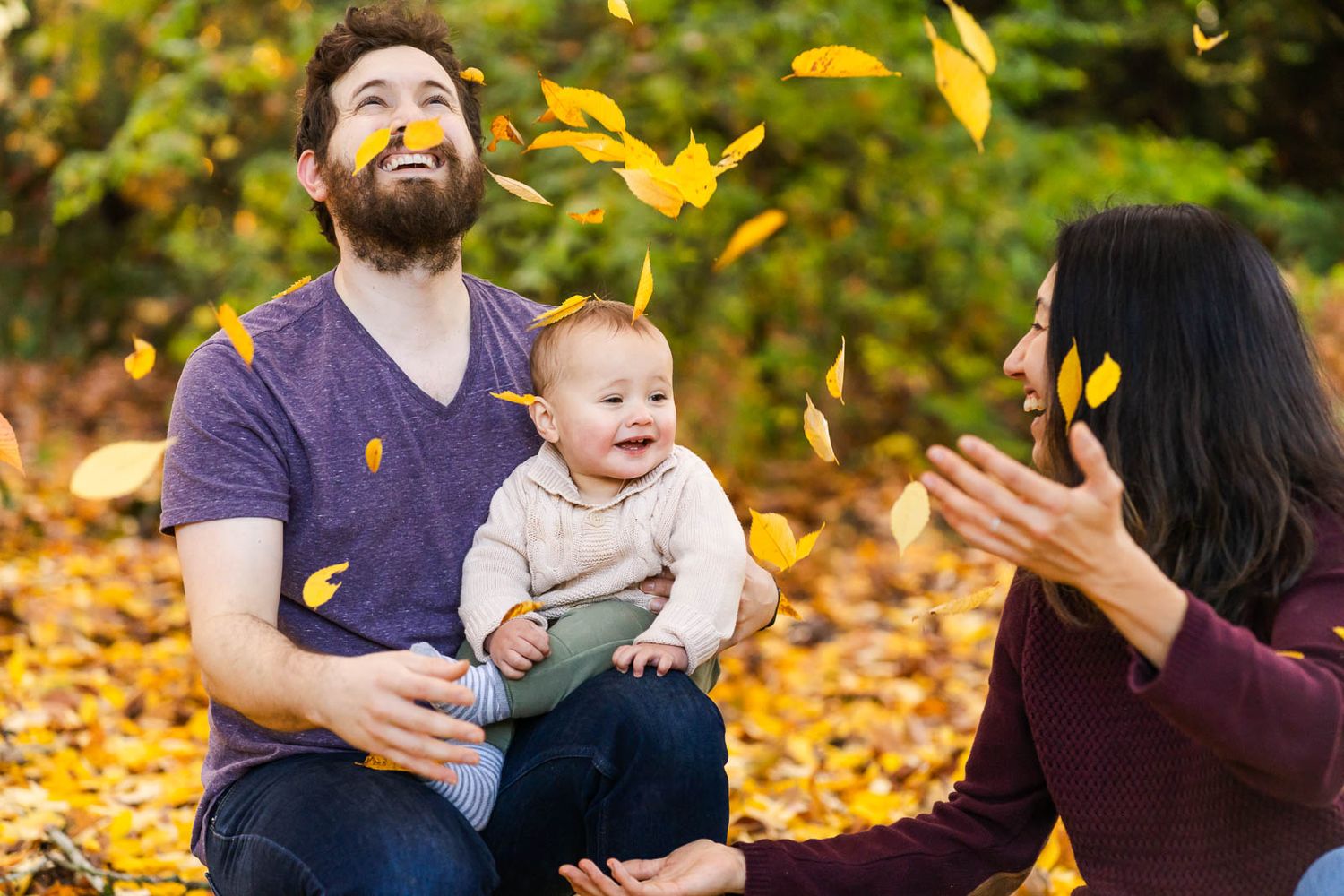Parents throw leaves into the air while baby boy watches.