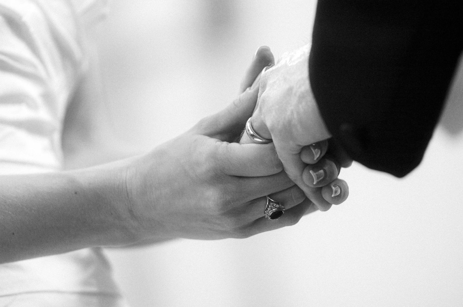 A close-up black and white photo of hands during a ring exchange ceremony.