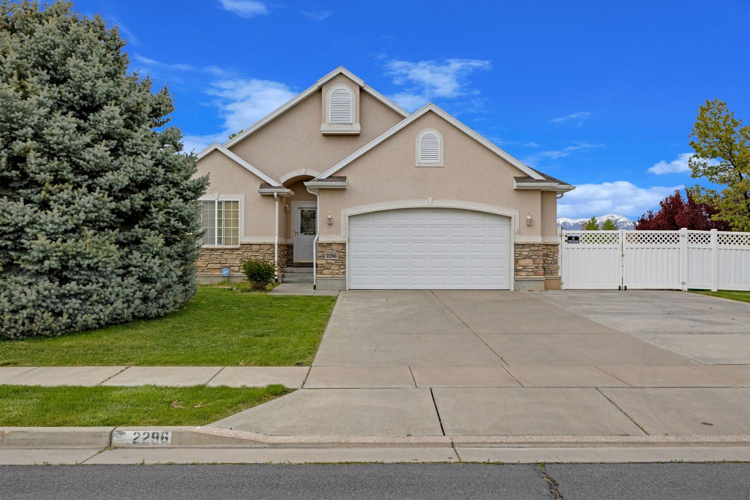 Two-story stucco home with stone accents, two-car garage, mature evergreen tree, and well-kept front lawn.