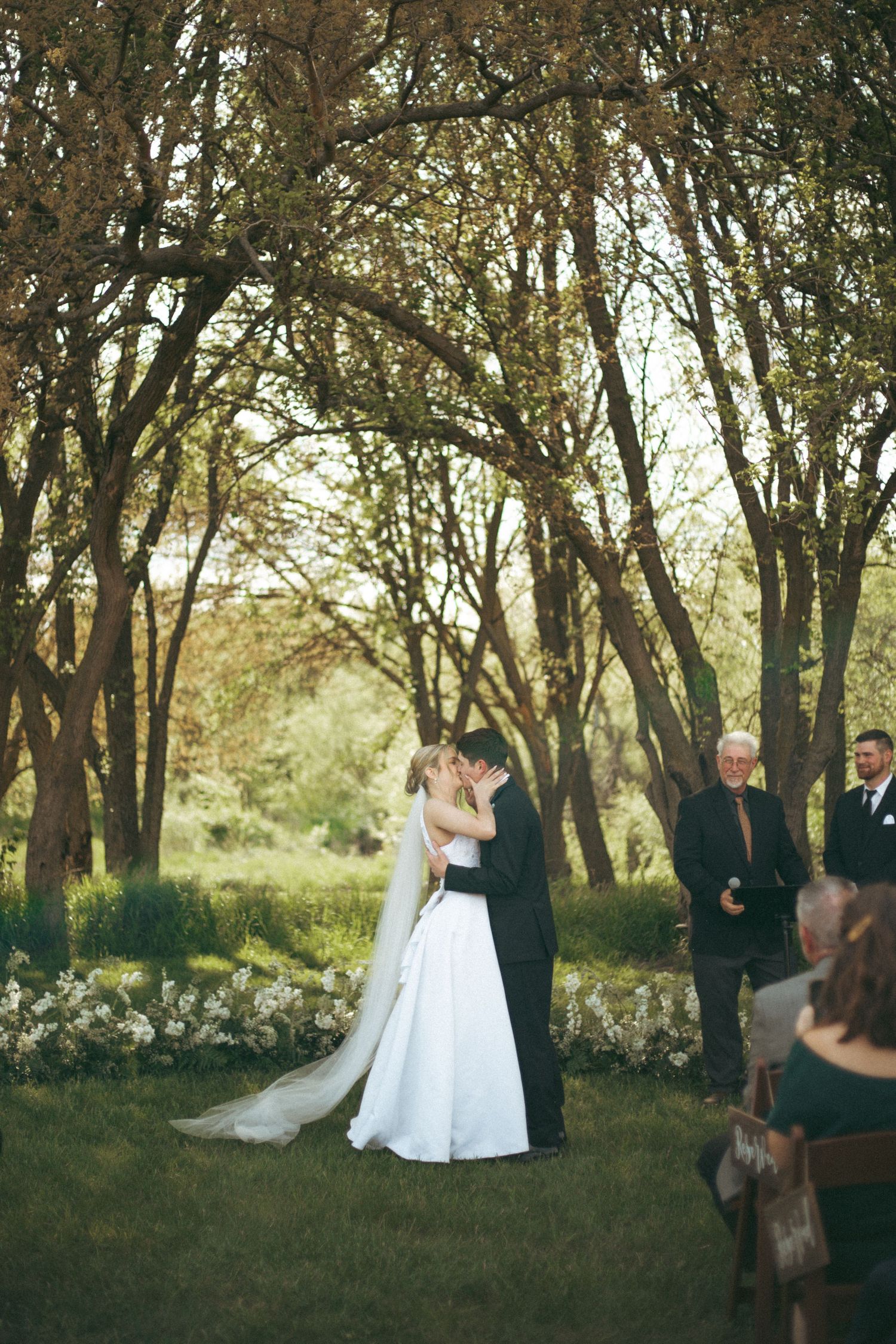 A couple shares a romantic moment during their woodland wedding ceremony as guests look on.