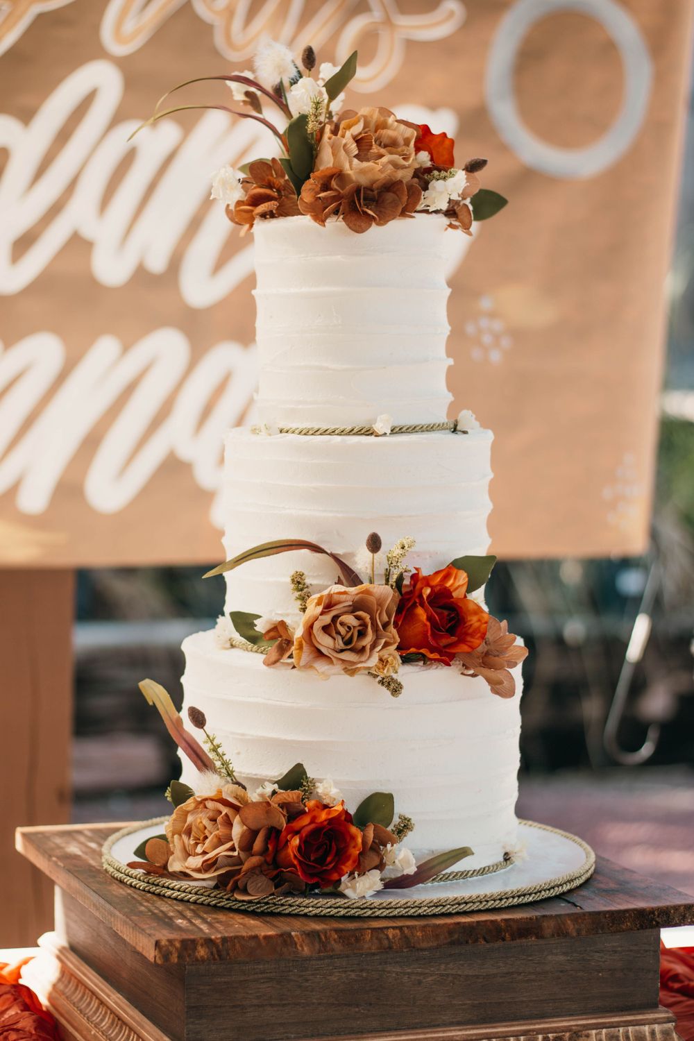 Elegant three-tier white wedding cake decorated with autumn-colored roses and florals.