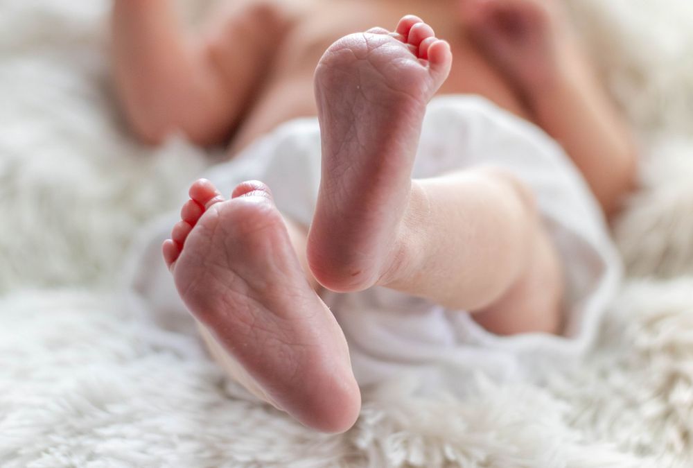 Tiny newborn baby feet against white fluffy blanket.