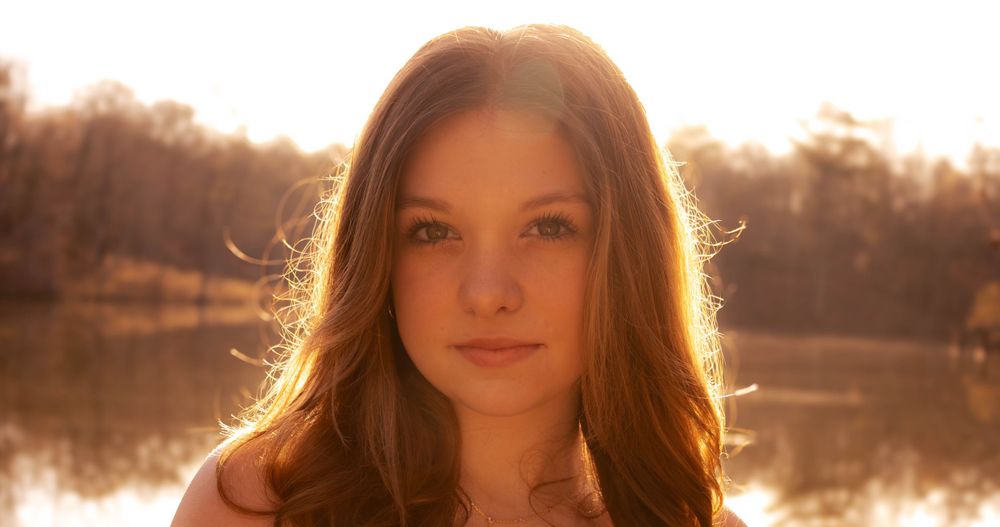 Portrait with backlit sunlit hair against a serene lake background in golden hour lighting.