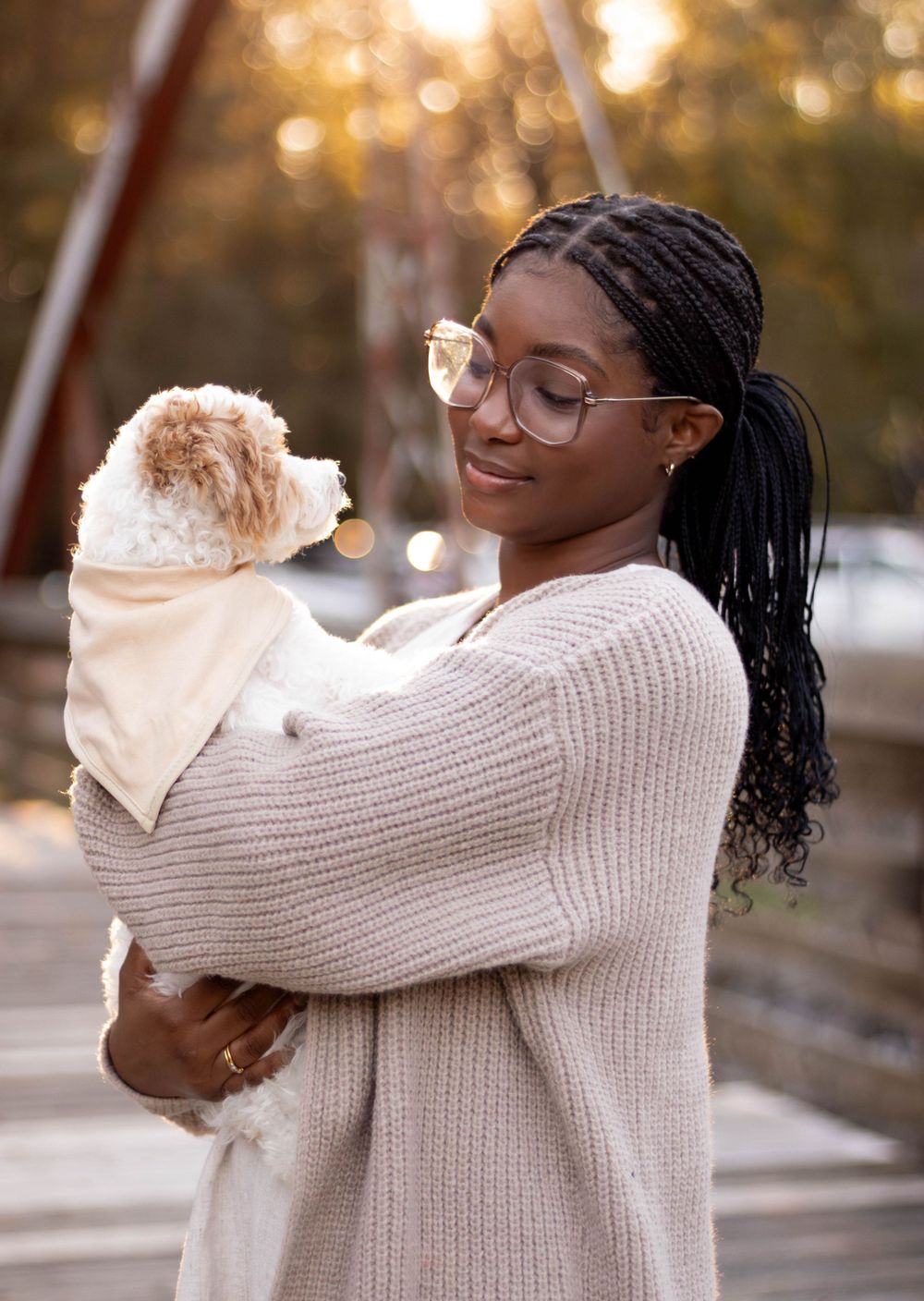 Person in cream sweater holding small white dog outdoors.