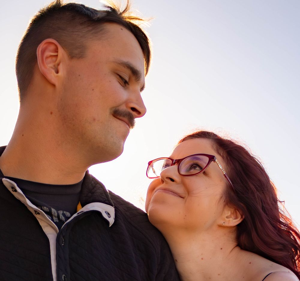 Romantic sunset portrait of couple with red hair against bright sky.
