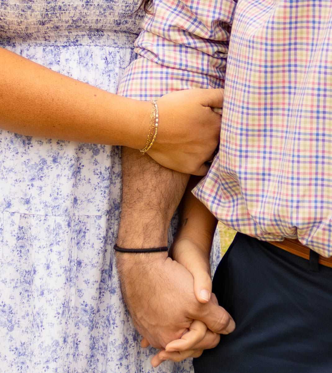 Close-up of couple holding hands showing delicate bracelet and plaid shirt details.