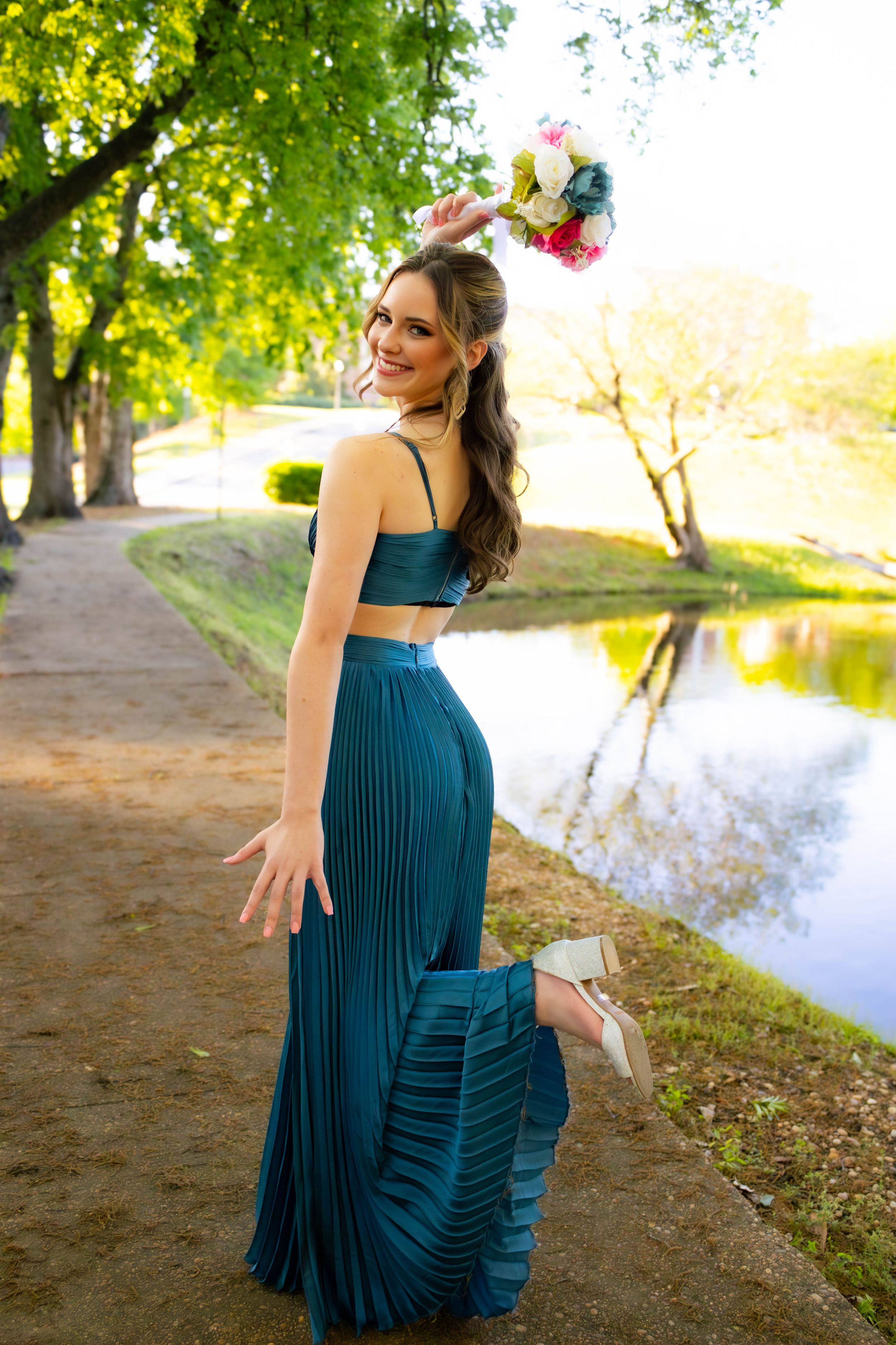 Woman in teal two-piece dress poses by lake during golden hour sunset.